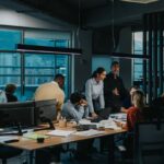 A diverse group of professionals collaborates in a modern office during an evening meeting.
