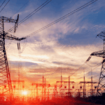 Silhouetted electrical transmission towers stand against a vibrant sunset sky.