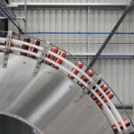 Cans moving along a curved industrial conveyor belt in a factory.