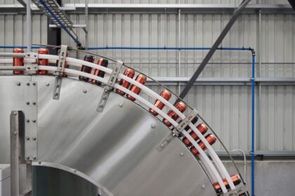 Cans moving along a curved industrial conveyor belt in a factory.