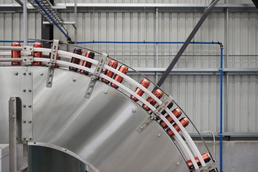 Cans moving along a curved industrial conveyor belt in a factory.