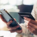 Close-up of a person holding a smartphone and a credit card for online shopping.