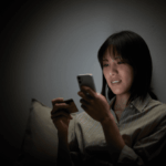 A woman shops online using her smartphone and a credit card in the dark.