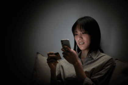 A woman shops online using her smartphone and a credit card in the dark.