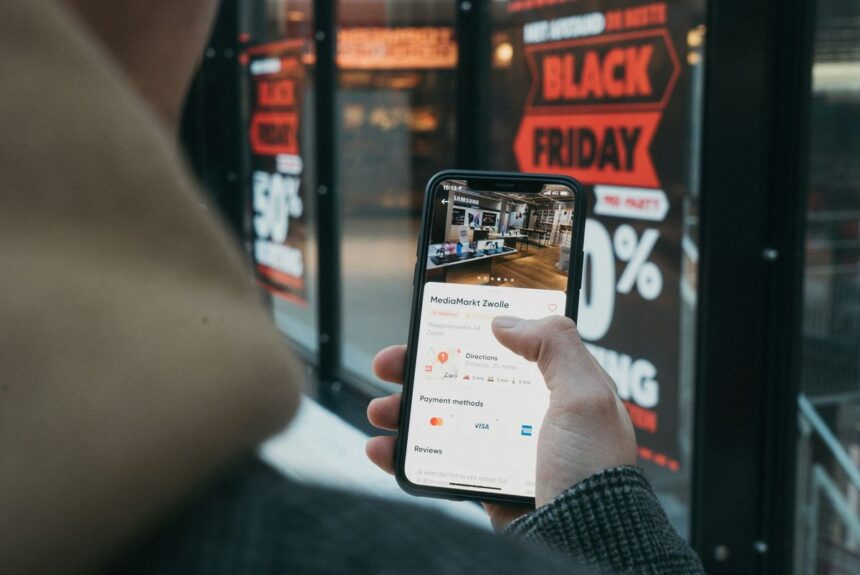 A person holding a smartphone showing a MediaMarkt store location in front of a storefront.