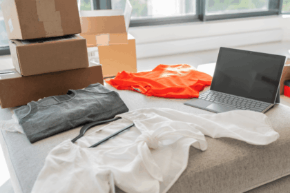 Clothing, shipping boxes, and a laptop arranged on a table for online retail processing.