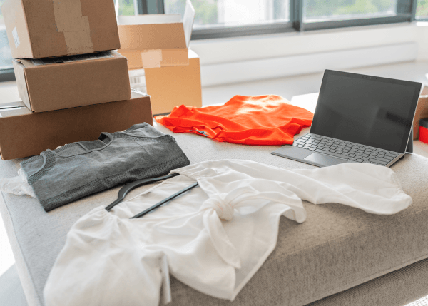 Clothing, shipping boxes, and a laptop arranged on a table for online retail processing.