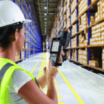 Worker in a hard hat and vest using a handheld barcode scanner in a warehouse.