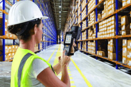 Worker in a hard hat and vest using a handheld barcode scanner in a warehouse.