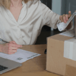 A person at a desk preparing a package for return with a form and laptop.