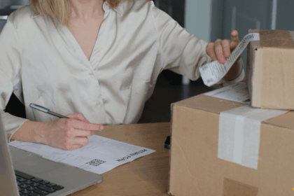 A person at a desk preparing a package for return with a form and laptop.