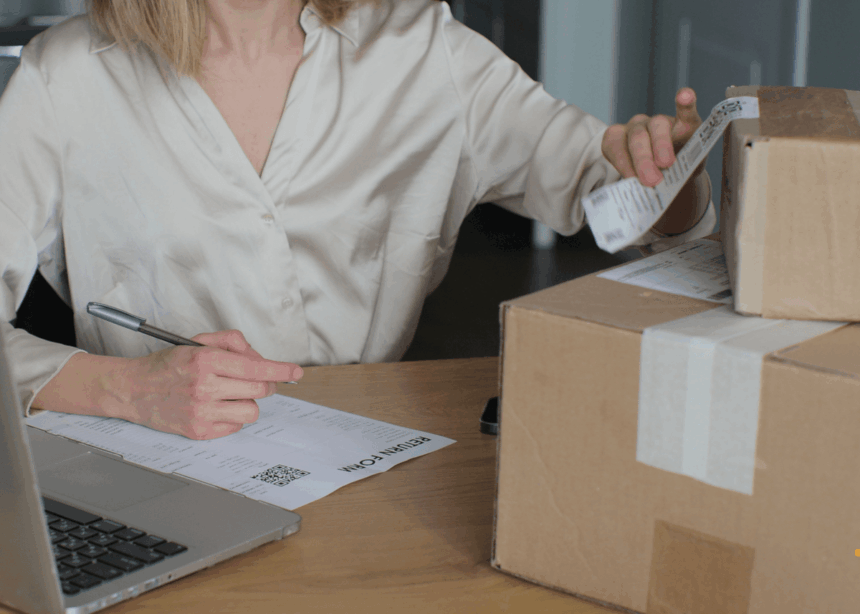 A person at a desk preparing a package for return with a form and laptop.