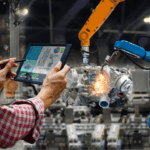 A person uses a tablet to monitor industrial robotic arms welding a car engine.