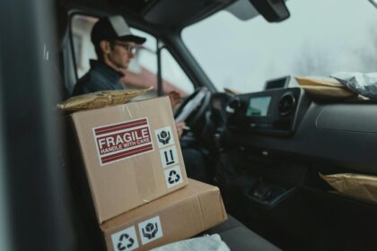 Delivery driver in a van with stacked cardboard packages, one marked Fragile.