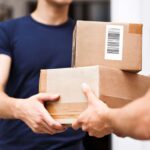 A delivery person handing a cardboard package to a recipient.