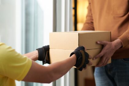 A delivery worker in gloves handing a cardboard box to a customer.