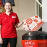 A smiling Coles employee recycling a plastic bag in a store collection bin.