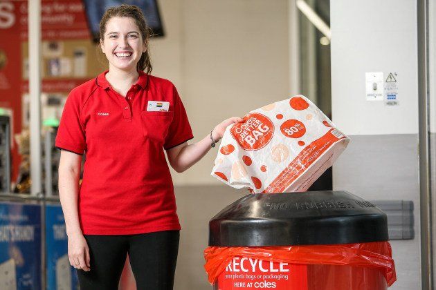 A smiling Coles employee recycling a plastic bag in a store collection bin.
