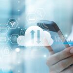 Hand holding a smartphone with digital cloud data synchronization and business icons overlay.