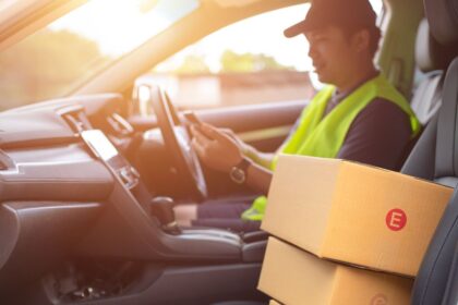 Delivery driver in a vehicle checking a smartphone with packages on the seat.