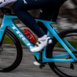 A cyclist rides a bright blue Trek road bike on an outdoor road.