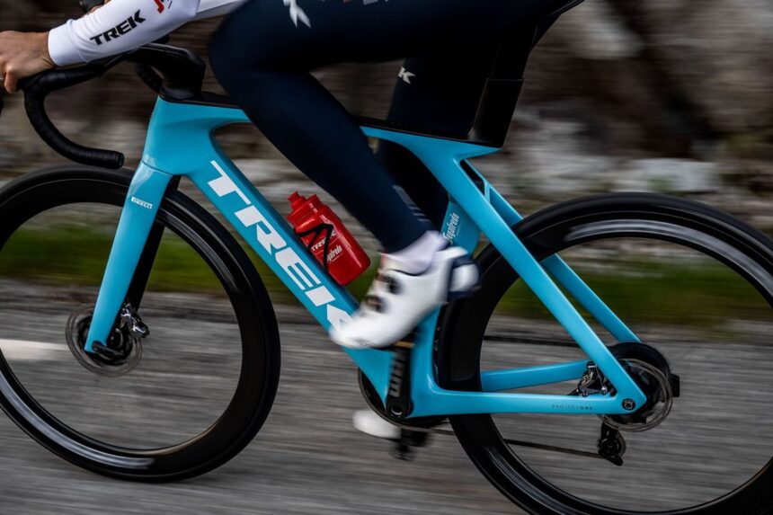 A cyclist rides a bright blue Trek road bike on an outdoor road.