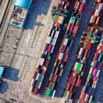 Aerial view of a busy shipping port with stacked containers and nearby water.