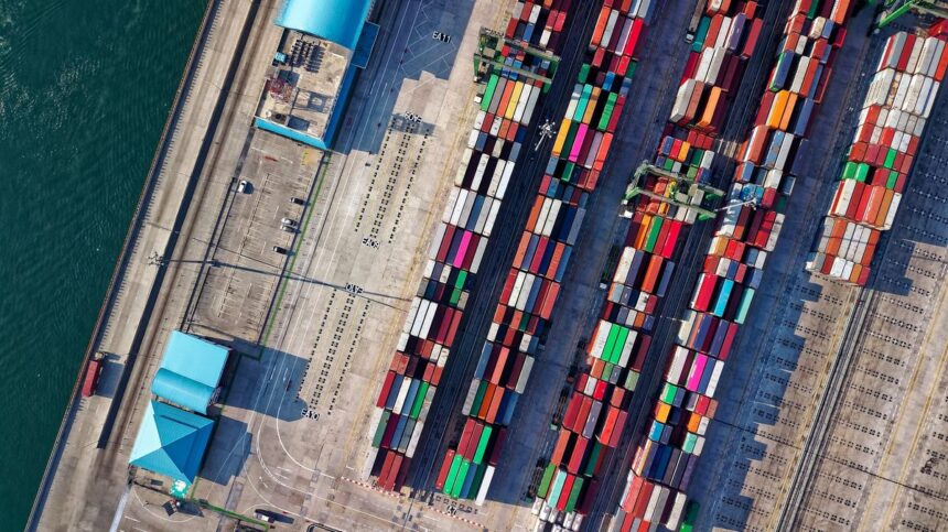Aerial view of a busy shipping port with stacked containers and nearby water.