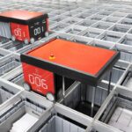 Two red AutoStore robots move across a grid of storage bins in a warehouse.