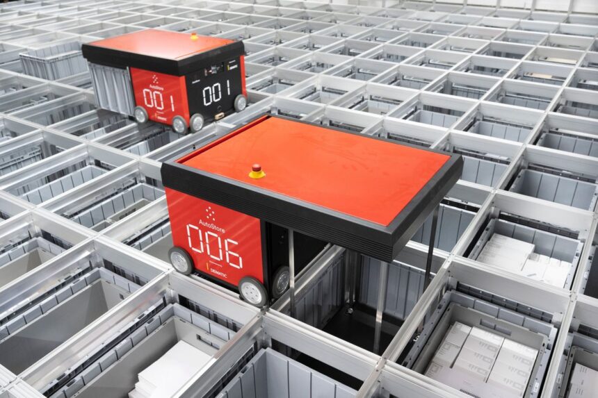 Two red AutoStore robots move across a grid of storage bins in a warehouse.