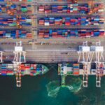 Aerial view of cargo ships being loaded with shipping containers at a busy port.