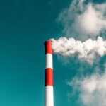 A red and white striped factory smokestack emitting thick smoke against a blue sky.