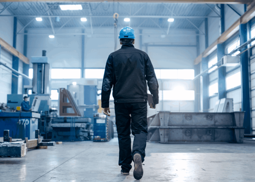 Worker in a hard hat walking through a large industrial manufacturing factory.