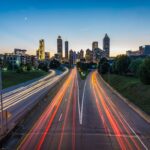 A highway with light trails leads toward the illuminated Atlanta city skyline at dusk.