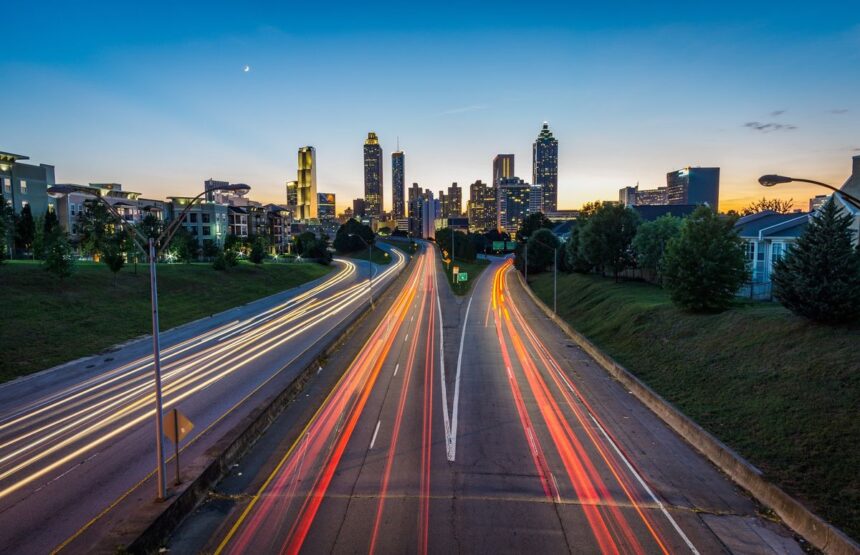 A highway with light trails leads toward the illuminated Atlanta city skyline at dusk.