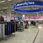 Interior of a retail store with a large blue please pay here sign overhead.