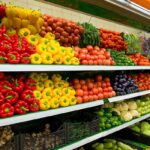 Shelves of a grocery store filled with fresh colorful peppers, tomatoes, and other produce.