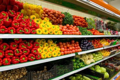 Shelves of a grocery store filled with fresh colorful peppers, tomatoes, and other produce.