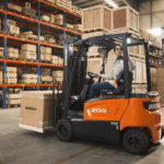 Operator driving a Doosan forklift carrying a cardboard crate in a warehouse.