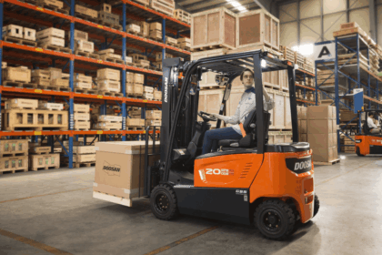 Operator driving a Doosan forklift carrying a cardboard crate in a warehouse.