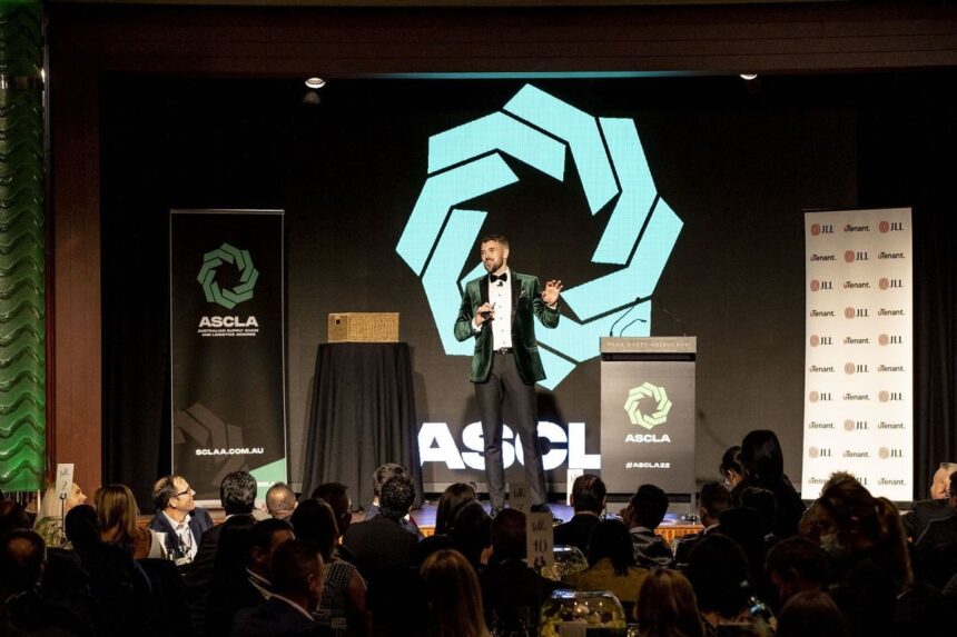 A man in a green velvet blazer speaks at an awards ceremony podium.