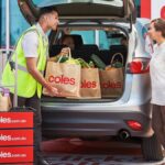 A Coles staff member loads groceries into the trunk of a customer's car.