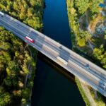 Aerial view of a highway bridge over a river surrounded by lush green trees.