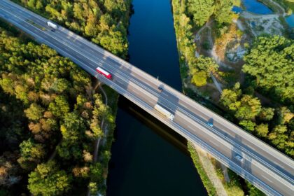 Aerial view of a highway bridge over a river surrounded by lush green trees.