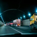 Cars and a semi-truck driving through a dimly lit highway tunnel at night.