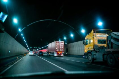 Cars and a semi-truck driving through a dimly lit highway tunnel at night.