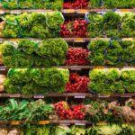 Shelves in a grocery store stocked with fresh lettuce, radishes, and root vegetables.