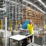 Warehouse workers in neon yellow shirts sorting clothing near automated shelving systems.