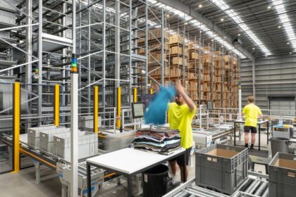 Warehouse workers in neon yellow shirts sorting clothing near automated shelving systems.