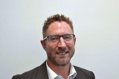A professional portrait of a man in a blazer and white shirt.